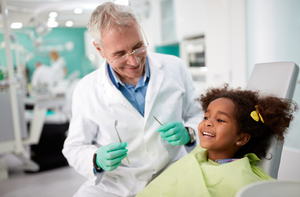 Girl smiling in a dentist chair with a smiling dentist next to her.