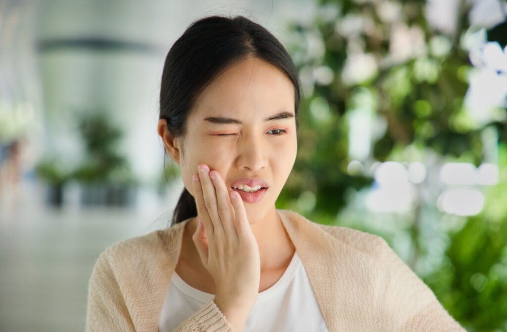 A young person holding their cheek due to a suddenly painful sensitive tooth.