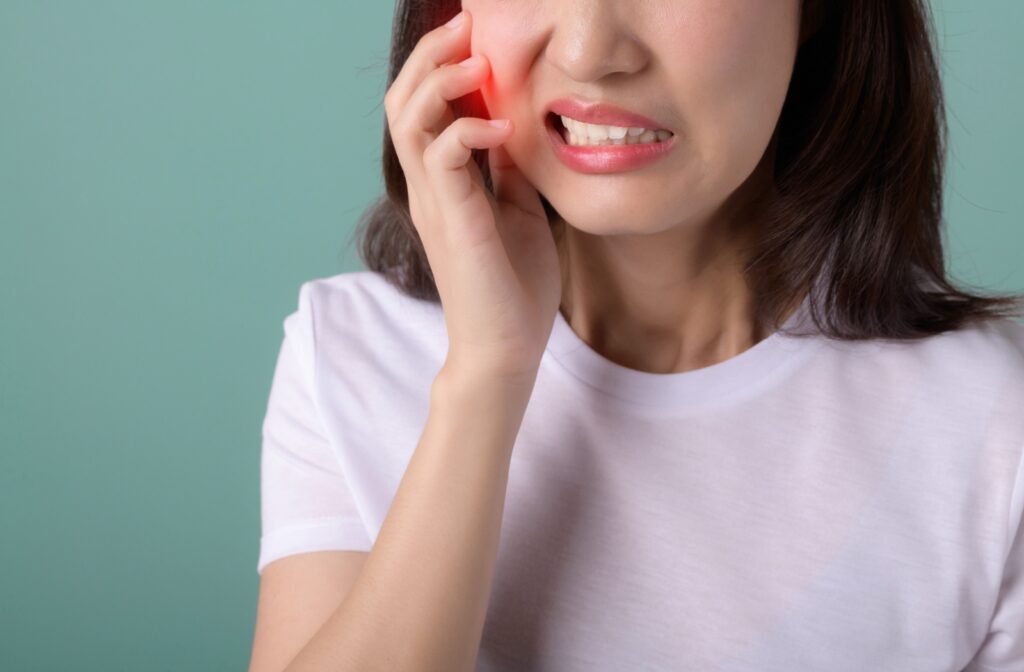 A person standing against a green background clutches their jaw as they experience sudden tooth pain