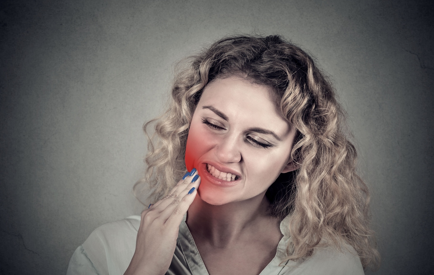 A person rubbing their sore jaw tenderly. They have a persistent toothache caused by an untreated cavity, visualized as a red gradient across their jaw.