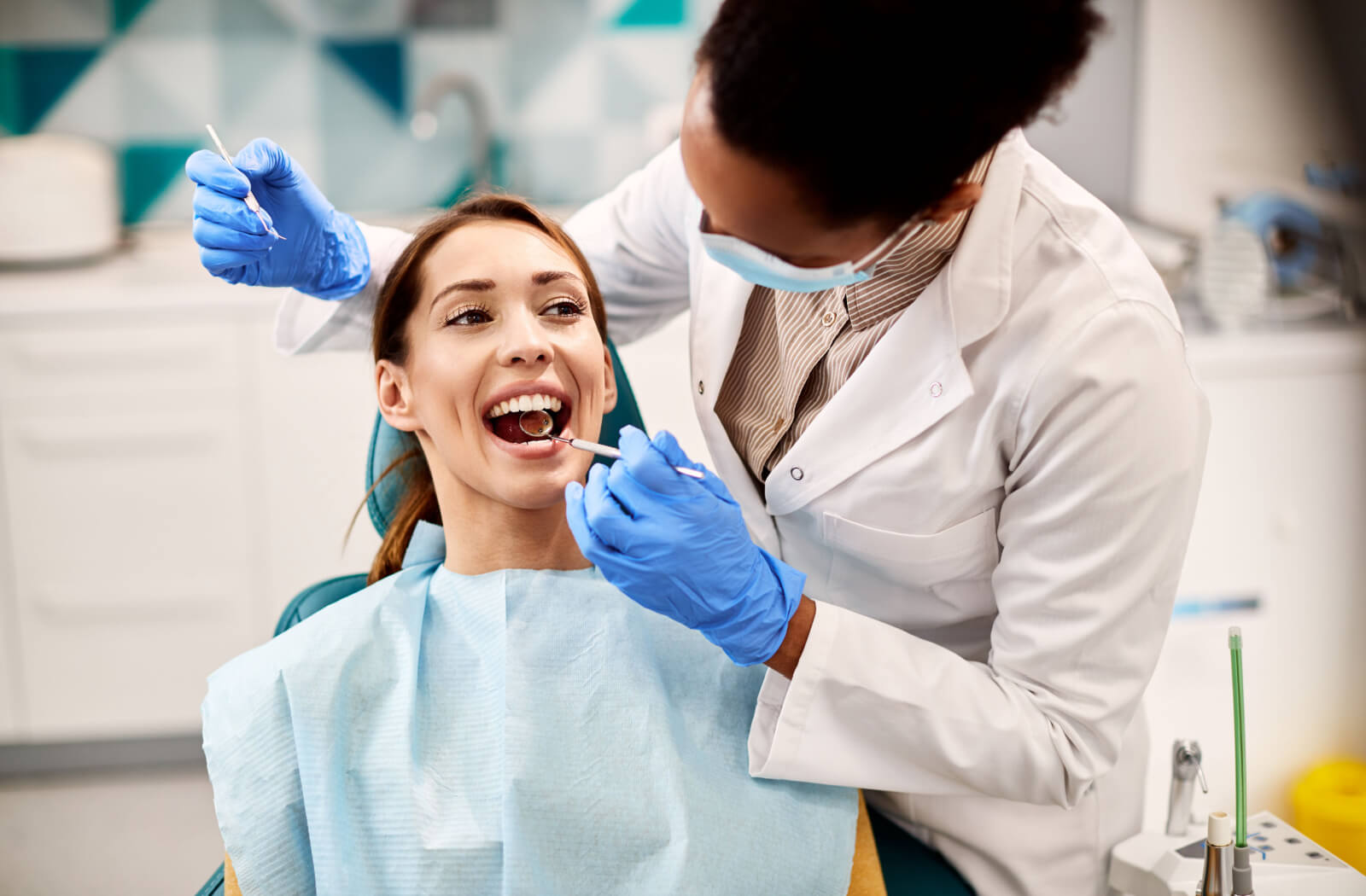 A dental patient smiling during their appointment while their dentist checks their teeth.