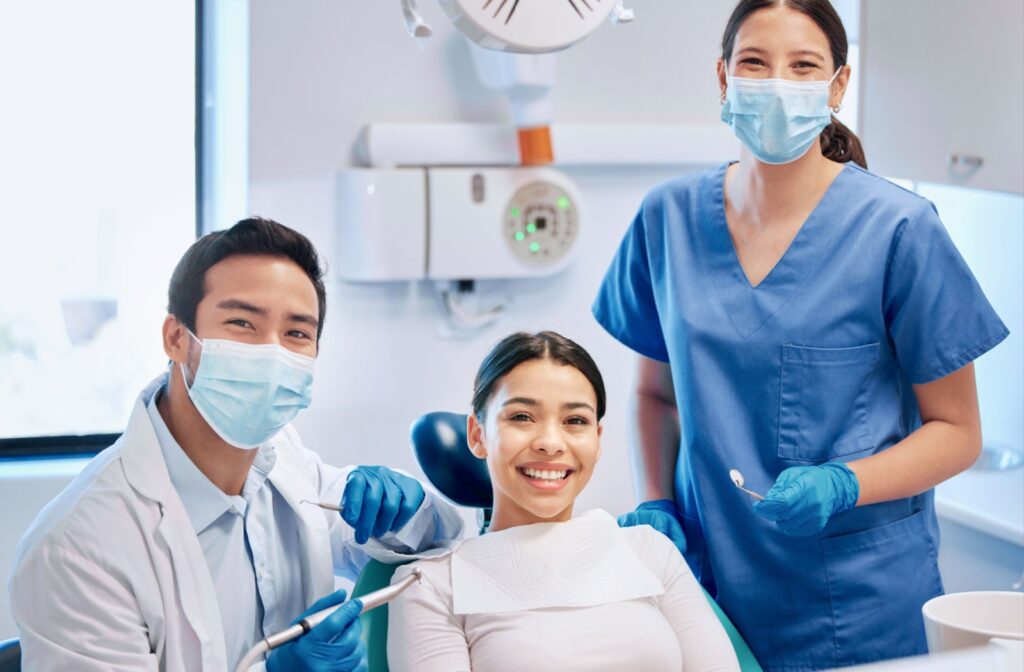 A patient smiles brightly at the end of their dental cleaning and exam with their dental team at their side.