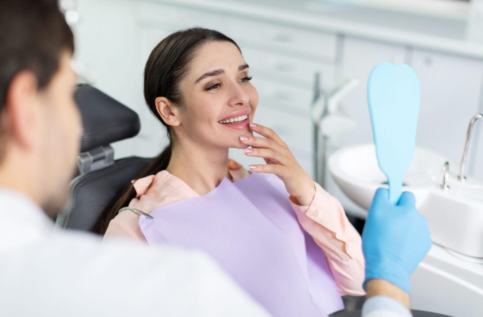 A dentist shows their patient their completed dental implants in a hand mirror.