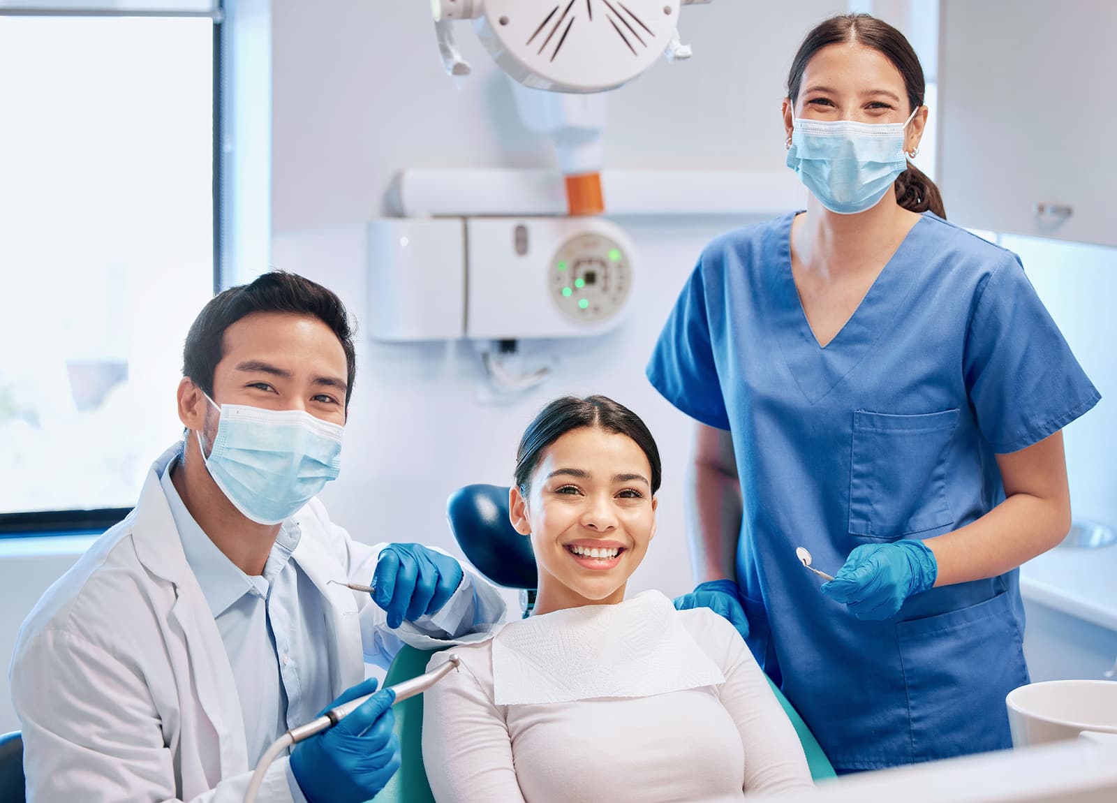 A patient smiles brightly at the end of their dental cleaning and exam with their dental team at their side.